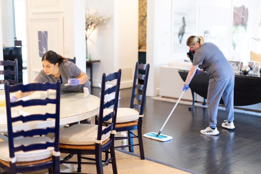 Professional cleaners wiping a dining table and mopping hardwood floors in a modern Manchester home during a house cleaning service.