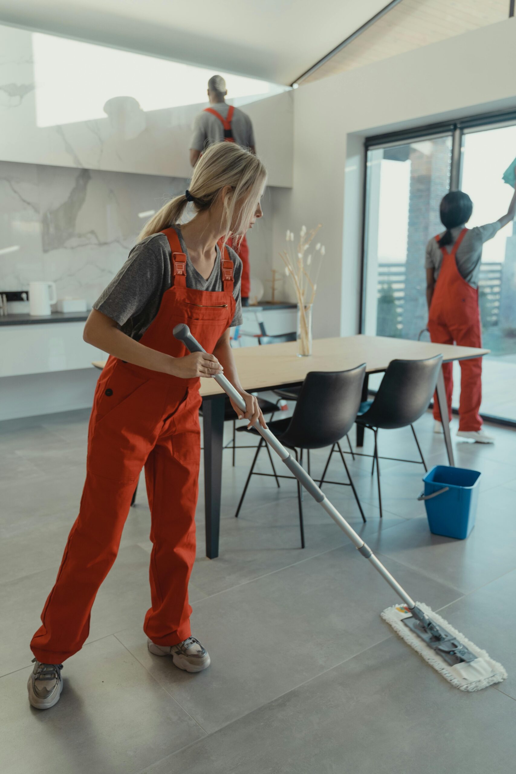 A team of professional cleaners from PJJ Cleaning Services in Manchester are actively mopping floors, cleaning windows, and reaching high areas in a spacious, modern commercial or residential property.