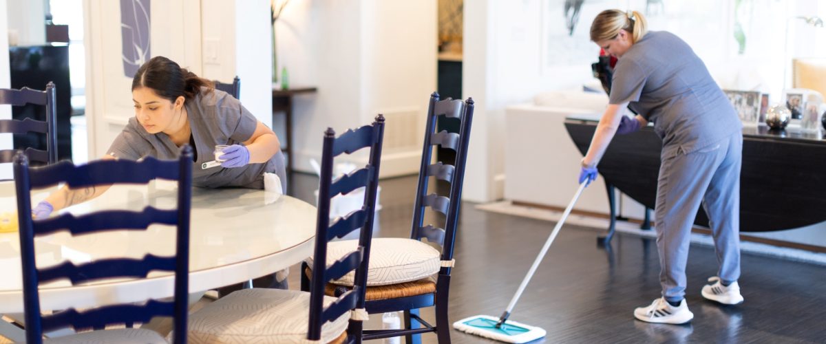 Professional cleaners wiping a dining table and mopping hardwood floors in a modern Manchester home during a house cleaning service.